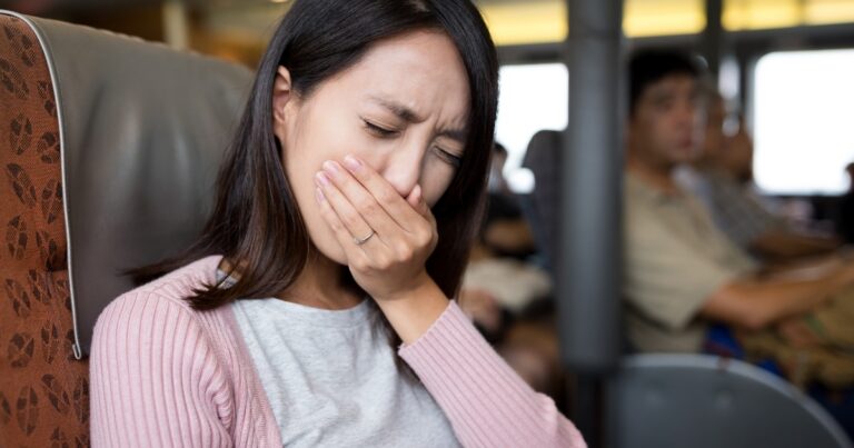 A Woman Sitting In A Train Appears To Be In Discomfort, Covering Her Mouth, Possibly Experiencing Tooth Pain. Explore Home Remedies To Instantly Relieve Tooth Nerve Pain.