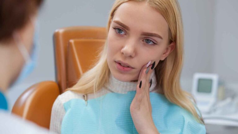 Woman Sitting In A Dental Chair Holding Her Cheek, Possibly Experiencing Tooth Pain, Seeking Home Remedies To Alleviate Nerve Discomfort.