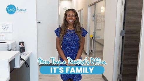 Emergency dentist in Katy, TX office interior with a smiling staff member in a blue dress, promoting family-friendly same-day and urgent dental care at Smile Avenue. Modern clinic hallway in the background highlights welcoming environment.