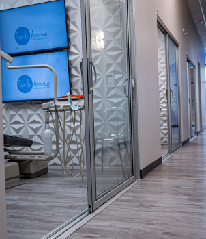 Modern dental office interior with sleek design, featuring glass partitioned treatment rooms and Smile Avenue branding on digital displays, in a Cypress TX family and cosmetic dentistry clinic.