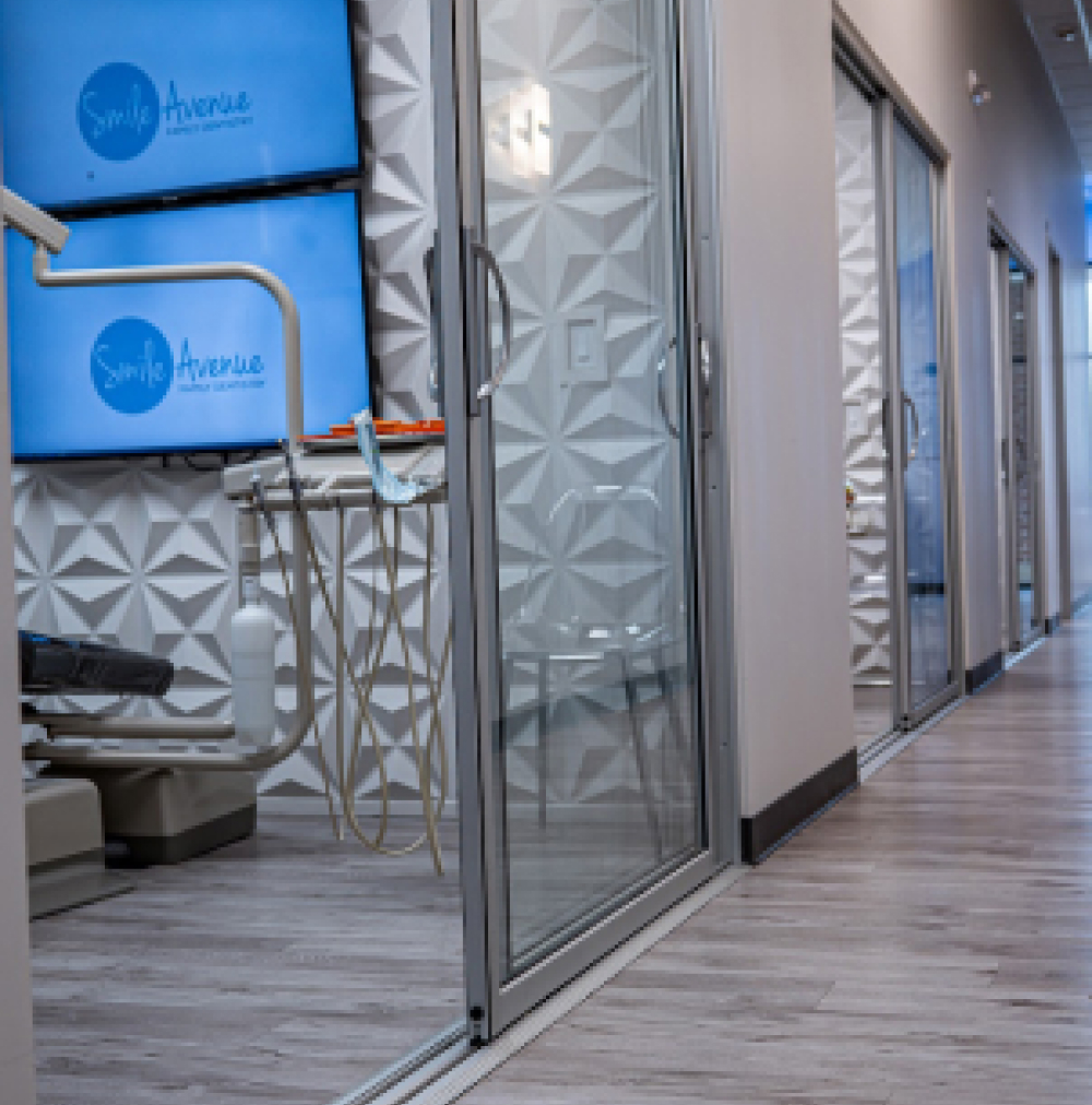 Modern dental clinic hallway at Smile Avenue, Cypress TX, featuring a clean, professional interior with dental equipment and glass doors.