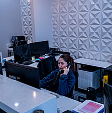 Reception area of Smile Avenue, a Cypress TX family dentist and cosmetic care office, showing a receptionist working at a desk with a computer and phone in a modern, geometric-wallpapered environment.