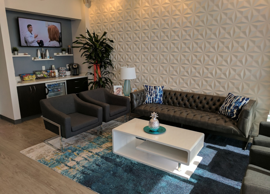 Modern dental office waiting room in Cypress, TX featuring sleek seating, a patterned accent wall, and a refreshment area with snacks and beverages, creating a welcoming environment at Smile Avenue Family and Cosmetic Dentistry.