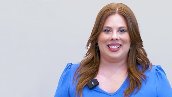Woman in blue blouse smiling, wearing a microphone clip, featured in Katy Dental's patient education video library.