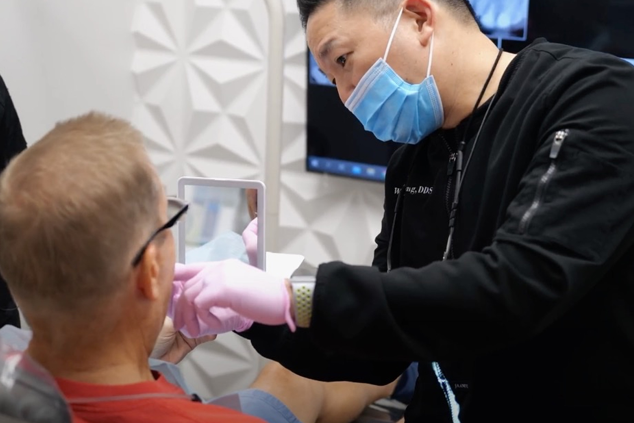 Dentist in a mask showing a dental patient a mirror during consultation at Smile Avenue Dentistry in Katy, TX, highlighting dental treatments.