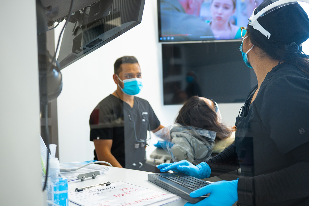 Dental professionals wearing masks and gloves attending to a patient in a modern dental office in Katy, TX, emphasizing cosmetic dentistry services including smile makeovers and veneers.
