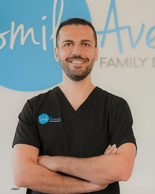 Dentist at Smile Avenue Family Dentistry in Cypress, TX, standing confidently with arms crossed in front of clinic sign.
