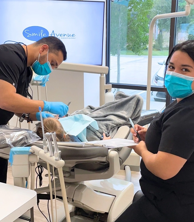 Family Dentistry in Cypress TX - Dentist and assistant providing dental care to a child patient in a modern clinic, focusing on prevention and gum disease care.
