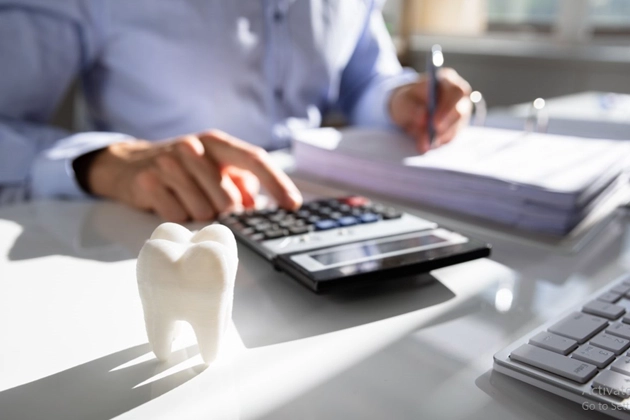 A person calculating finances with a calculator and a notebook on a desk, alongside a dental tooth model, representing dental financing and payment plans at Smile Avenue Cypress.