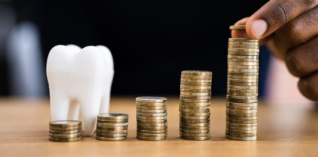 A stack of coins arranged in ascending order next to a model of a tooth, symbolizing affordable dental coverage and financial planning. A person's hand is adding coins to the tallest stack, representing increasing savings or dental payment plans.