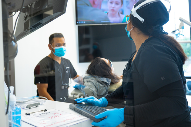 Dentist and assistant using advanced dental technology with a patient in a modern clinic in Katy. Both wearing masks and gloves for safety.