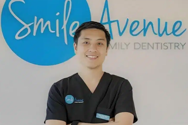 Dr. Kim, a dentist at Smile Avenue Family Dentistry in Katy, TX, is smiling and wearing black dental scrubs. He stands confidently in front of a wall with the Smile Avenue logo, embodying professional family and cosmetic dental care.