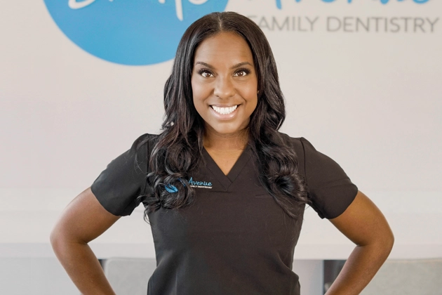 Female dentist in black scrubs smiling confidently at dental clinic, representing expert family and gum health services.