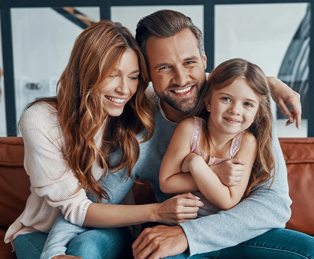 Happy family sitting together on a sofa, smiling warmly, symbolizing care and trust in family dental services in Cypress, TX.
