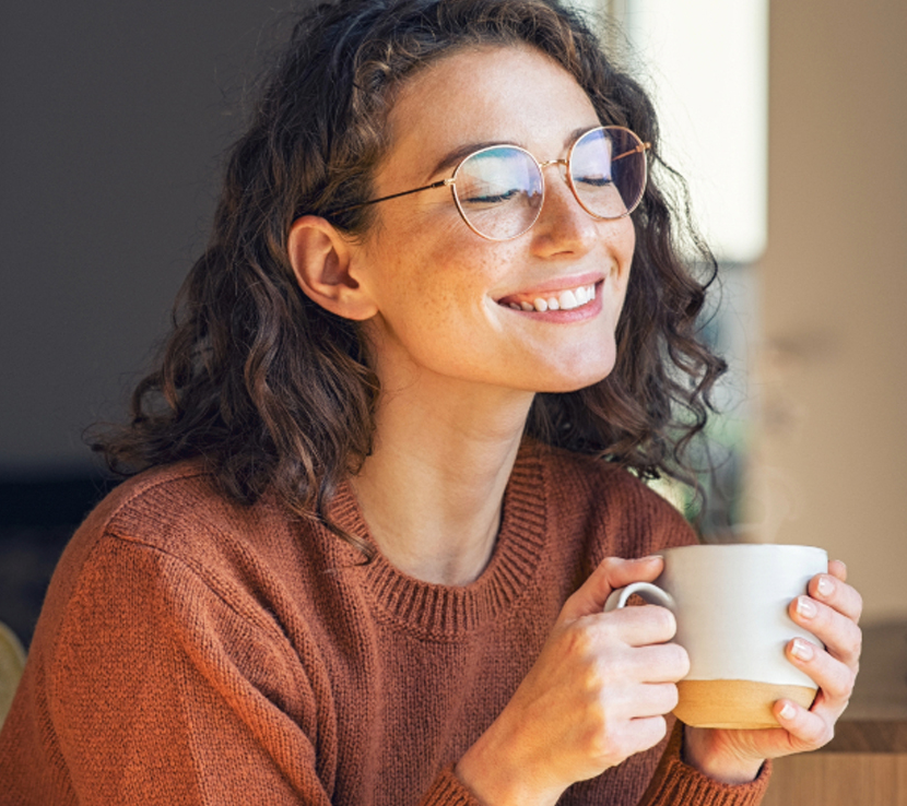 Smiling woman with glasses enjoying a cup of coffee, highlighting healthy dental care and general dentistry in Katy, TX.