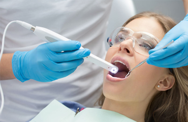 A dentist using advanced dental technology to examine a patient's teeth in Katy, featuring close-up of a female patient wearing protective glasses while undergoing an oral check-up with innovative tools.