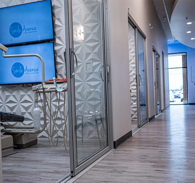 Modern dental office interior in Cypress, TX featuring sleek, contemporary design with glass doors and dental equipment. The hallway has wood-style flooring and geometric wall patterns, embodying family and cosmetic dental care ambiance.