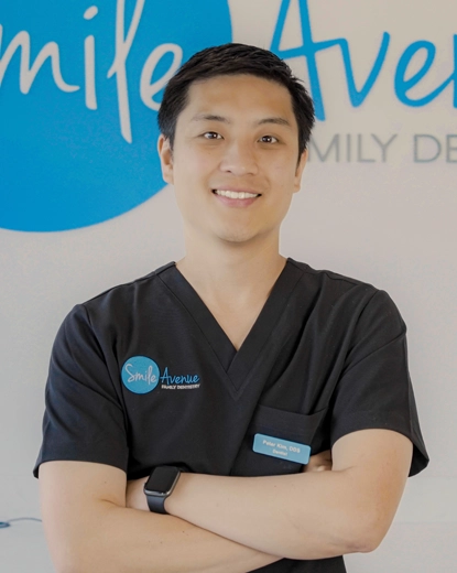 A dentist in black scrubs with crossed arms smiles confidently at Smile Avenue Family Dentistry in Katy, showcasing professional dental care.