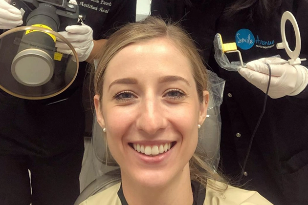 Woman smiling with bright teeth at a dental office in Cypress, surrounded by dental staff holding photography equipment, showcasing results of cosmetic dentistry.