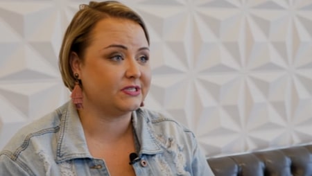 Woman with short hair and denim jacket sharing her smile makeover story at Smile Avenue Katy, sitting in front of a geometric patterned wall.