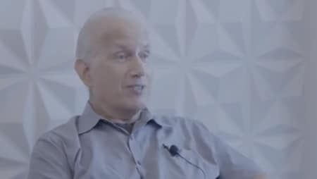 A person with a microphone attached to their shirt sits against a textured wall backdrop, appearing to be in conversation or interview setting. The image is related to inspiring smile makeover stories from Smile Avenue Katy.