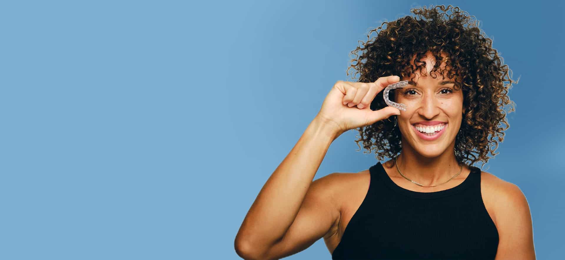 Invisalign Aligners1 1 Woman Holding A Clear Invisalign Aligner Near Her Face And Smiling