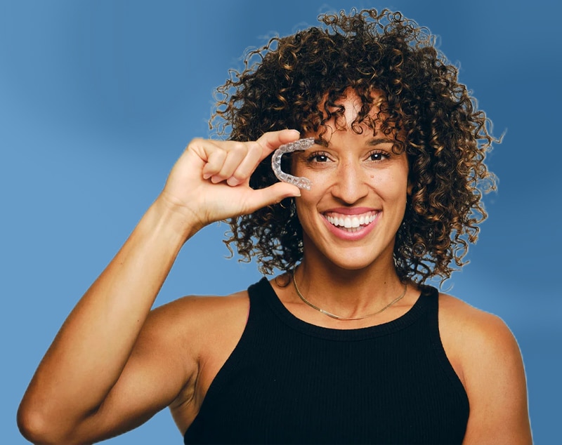 Invisalign Aligners1 2 Young Black Woman With Curly Hair Holding Invisalign Aligners And Smiling