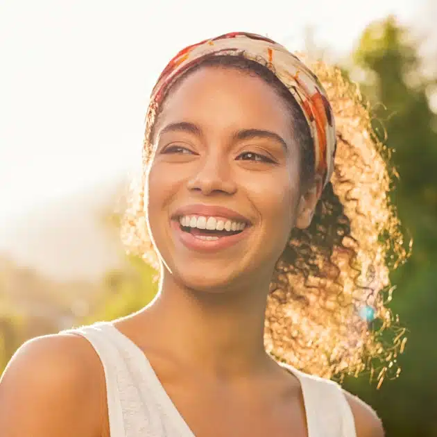 Emergency Dentist Katy, TX OLD1 2 Woman with natural hair smiling warmly in soft outdoor light