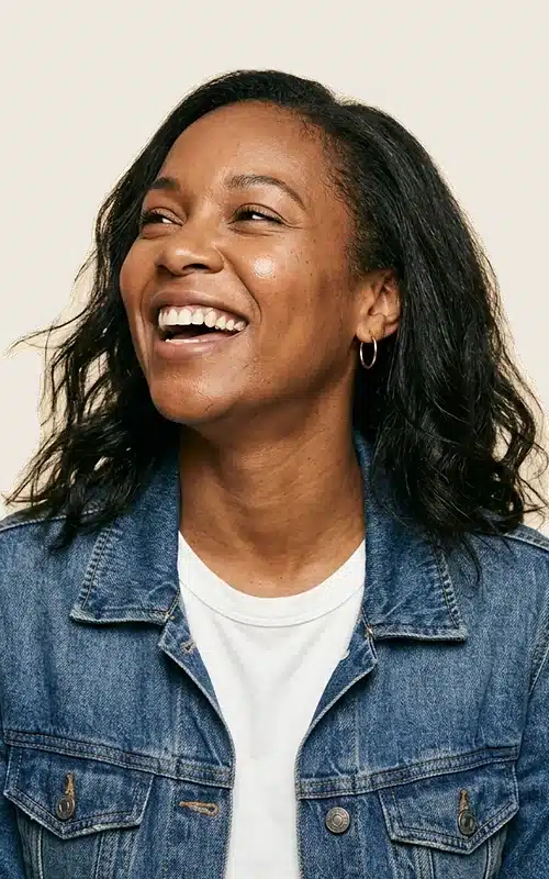A woman laughing, photographed against a warm cream background.